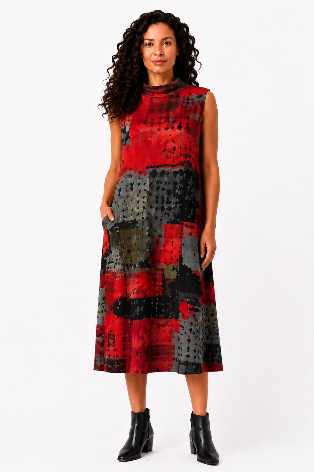 A woman modeling a sleeveless midi dress with an abstract patchwork pattern in red, black, and gray, paired with black ankle boots, against a plain white studio background.