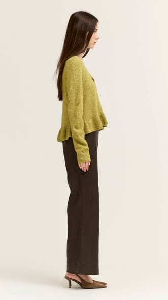 A woman shown in side profile wearing a cropped, textured olive green sweater and dark brown wide-leg trousers against a plain light background.
