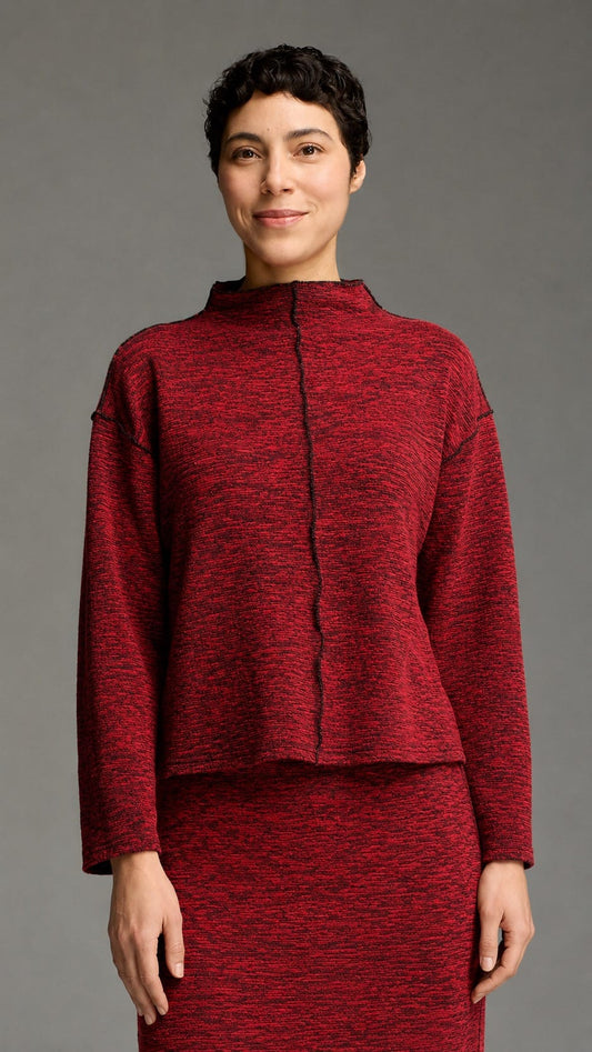 A model wearing a textured red and black knit two-piece set consisting of a cropped long-sleeve top with a mock neck and a matching skirt, shot against a solid gray studio background.
