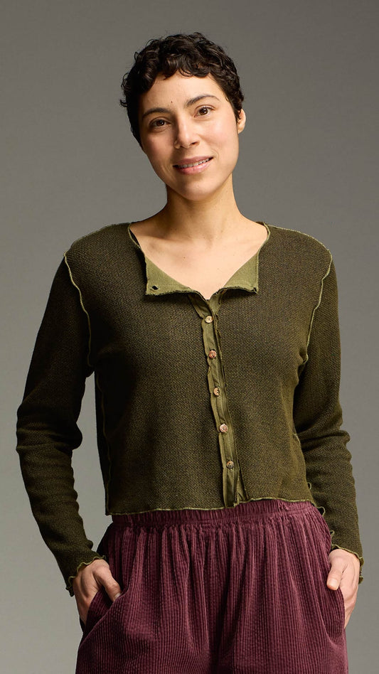 A woman modeling a dark olive green knit cardigan with a contrasting light olive green collar and button placket, paired with a burgundy skirt, against a solid gray studio background.