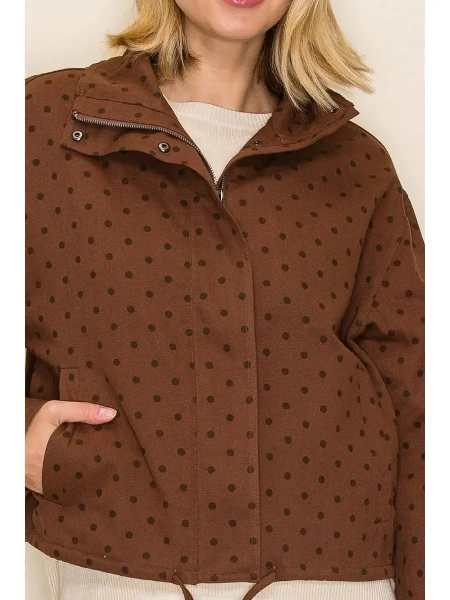 A close-up of a woman wearing a brown jacket with a black polka dot pattern, featuring a high collar, zipper closure, and front pockets.