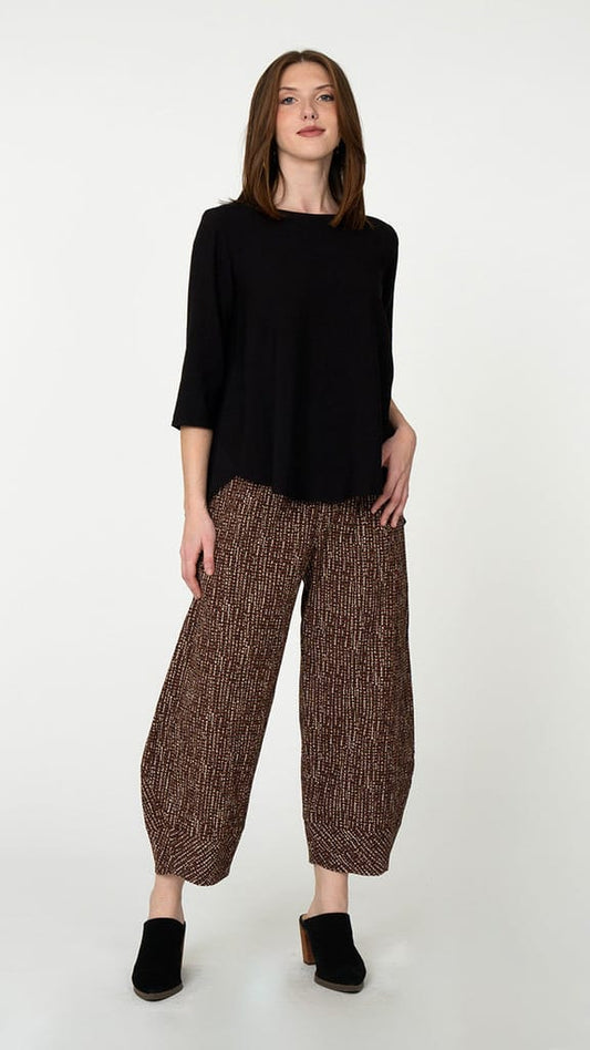 A woman modeling a black three-quarter sleeve top and brown patterned wide-leg cropped pants with black mule shoes, standing against a plain light gray studio background.