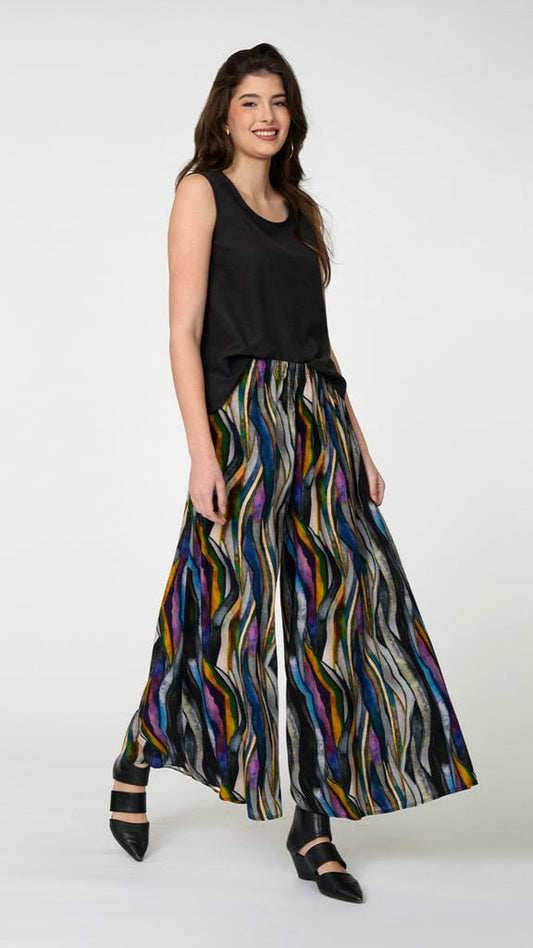 A woman modeling a sleeveless black top and a wide-leg, high-waisted pants with a vibrant multicolor wavy stripe pattern, set against a plain light gray studio background.