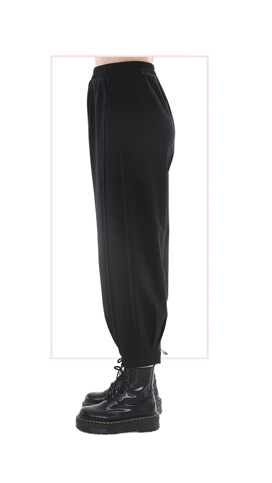 Black tapered barrel leg pants with an elastic waist shown on a model from the waist down wearing black lace-up boots against a white background with a faint pink rectangular outline.