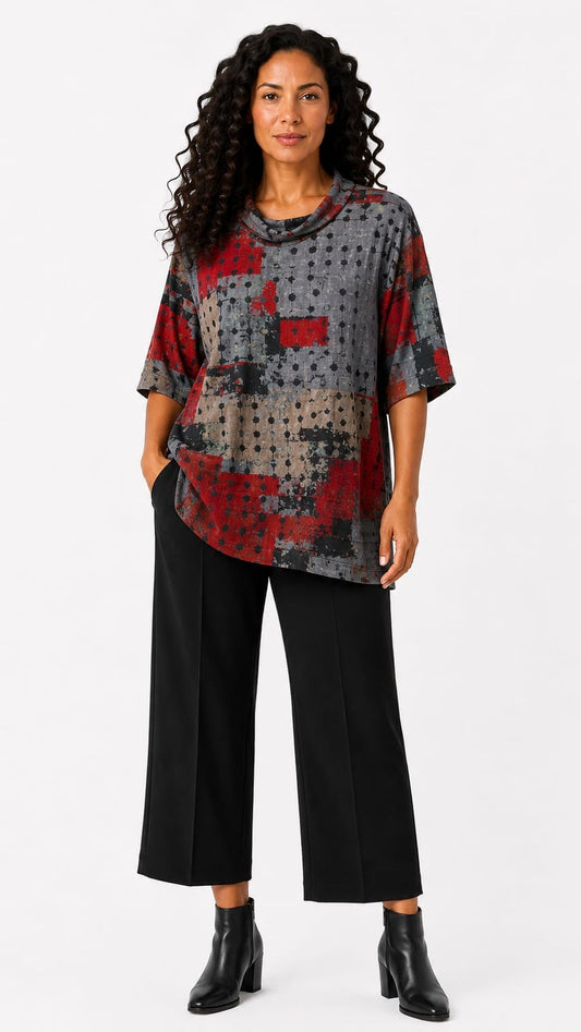 A woman modeling a short-sleeve abstract print top with red, gray, and beige tones, paired with black wide-leg cropped pants and black ankle boots, against a light gray studio background.