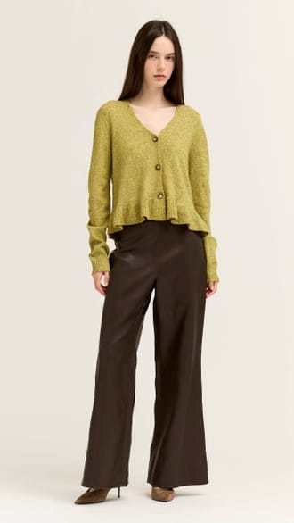 A woman modeling a cropped olive green cardigan with a V-neck and three front buttons, paired with dark brown wide-leg trousers, against a plain light background.