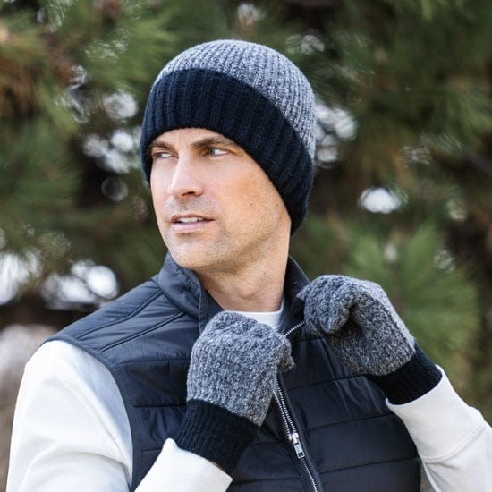 Man wearing a knit hat, gloves, and a vest outdoors with trees in the background