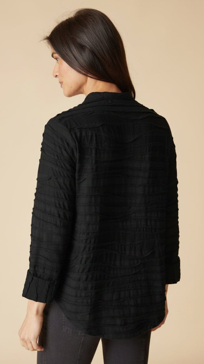 A woman shown from the back wearing a black textured, vertically pleated long-sleeve blouse against a solid beige background.