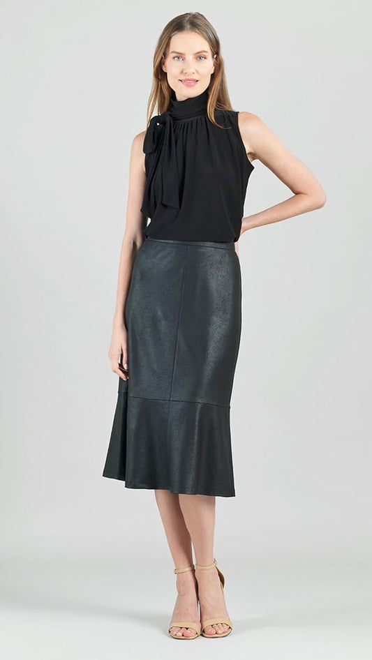 A woman modeling a sleeveless black mock-neck top with a large bow detail on the chest and a black faux-leather midi skirt with a ruffled hem, paired with beige high-heeled sandals, against a light gray studio background.