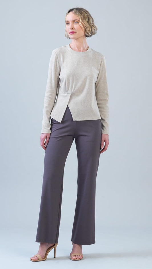 A woman modeling a light beige knit long-sleeve top with a wrap-style front detail and dark gray wide-leg trousers, standing against a light gray studio background.