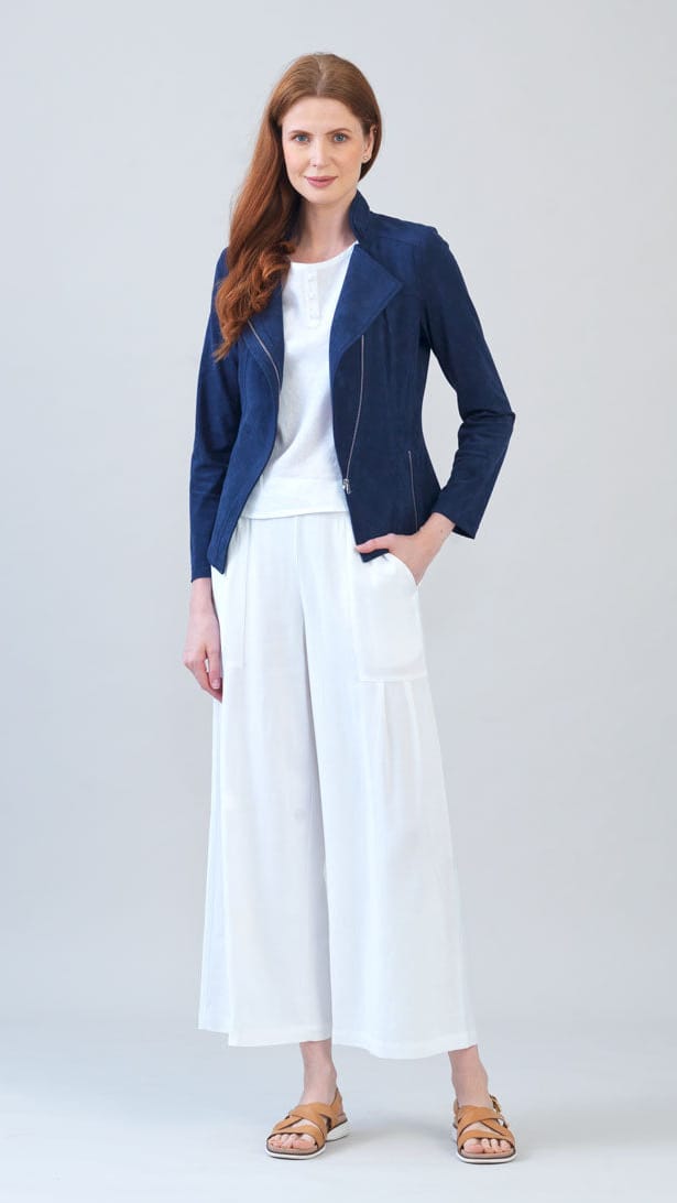 A woman modeling a navy blue zip-up jacket over a white top and white wide-leg cropped pants, paired with tan sandals, against a light gray studio background.