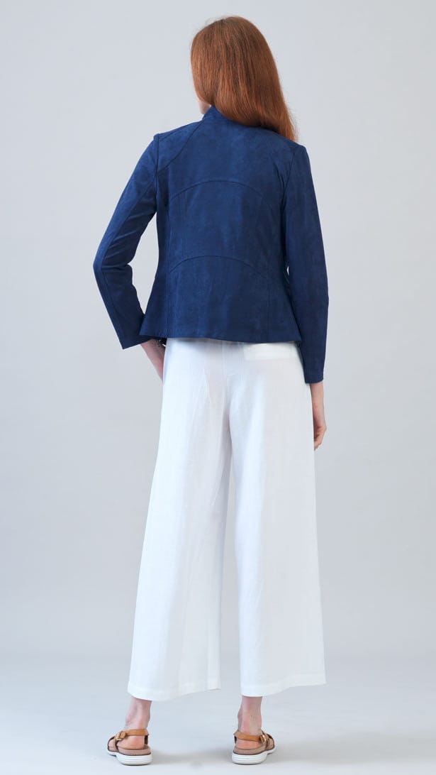 A woman stands with her back to the camera wearing a dark blue cropped jacket and white wide-leg cropped pants, paired with brown sandals, against a light gray studio background.