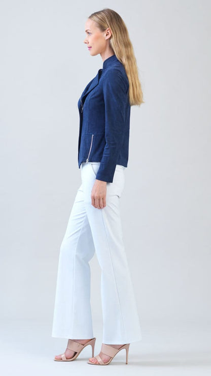 A woman stands in profile wearing a navy blue moto-style jacket, white wide-leg pants, and nude high-heeled sandals against a light gray studio background.