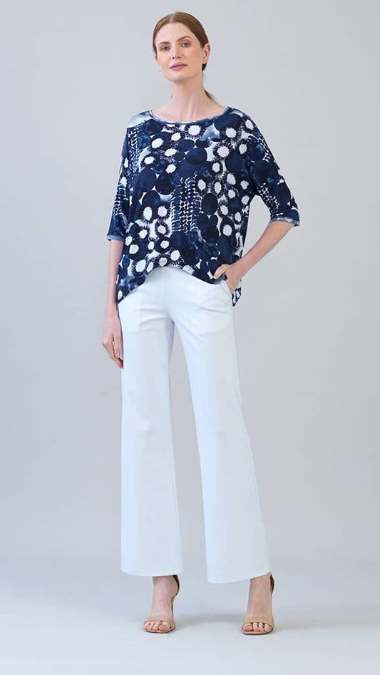 Woman wearing a blue patterned top and white pants on a gray background