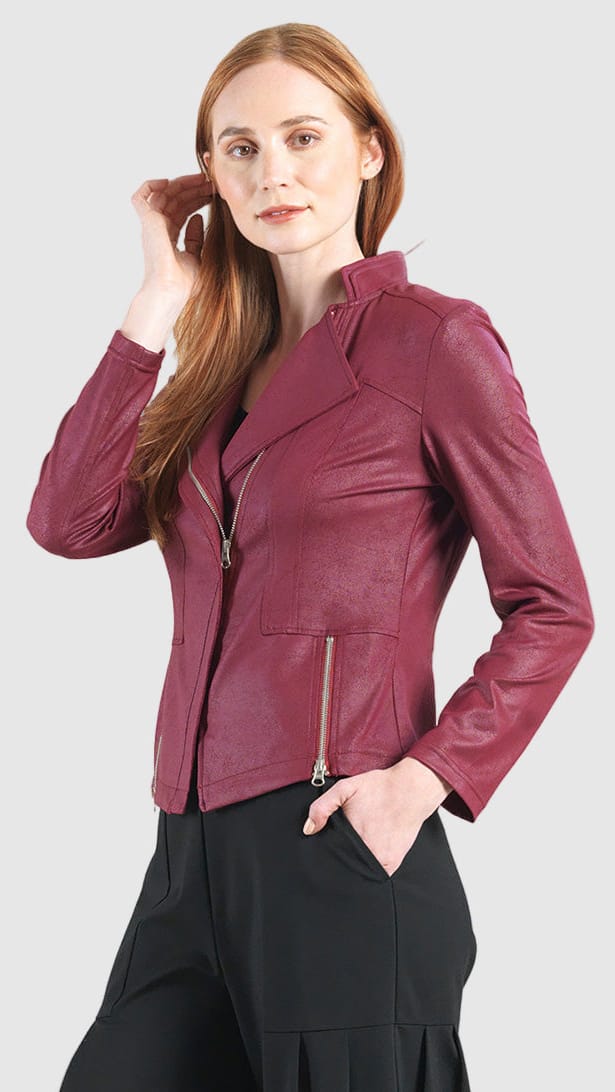 A woman modeling a burgundy faux-leather moto jacket with silver zippers, paired with black trousers, against a solid light gray background.