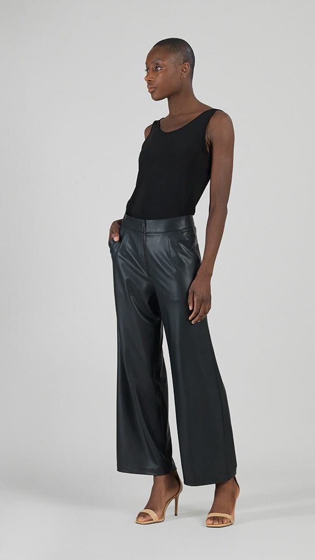 A model stands in profile wearing a black sleeveless top and black faux leather wide-leg trousers against a light gray studio background.