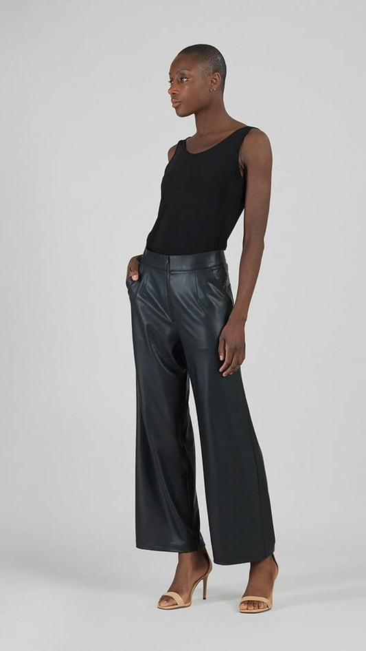 A model stands in profile wearing a black sleeveless top and black faux leather wide-leg trousers against a light gray studio background.
