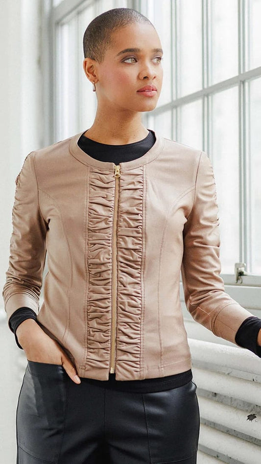 Woman wearing a beige leather jacket with black accents in an indoor setting.