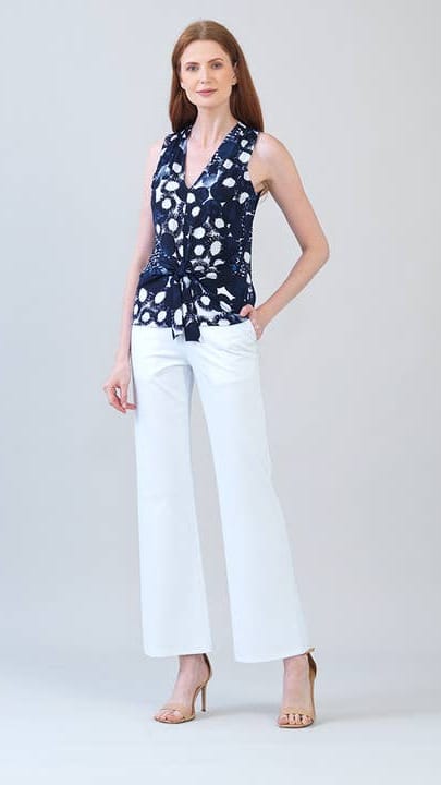 Woman wearing a navy sleeveless top with white polka dots and white pants on a light gray background