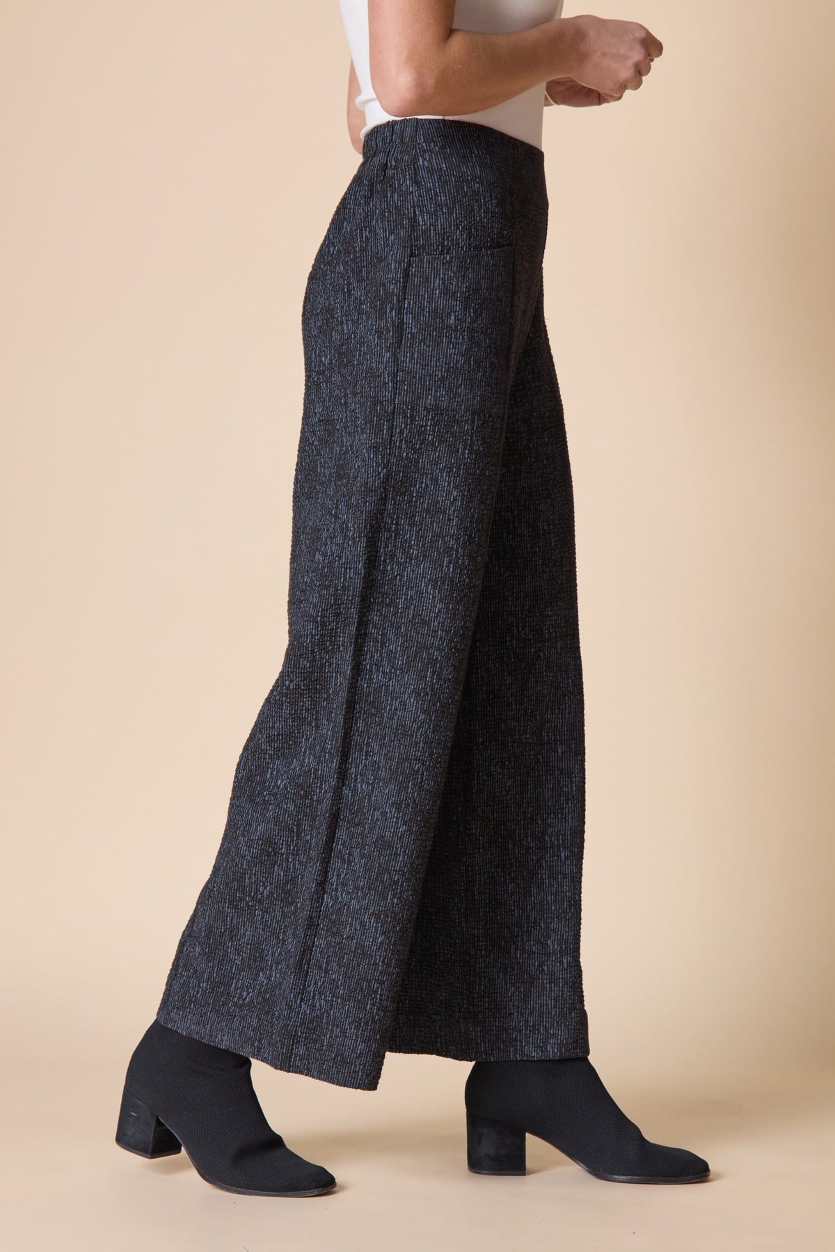 Person wearing dark gray wide-leg pants on a beige background