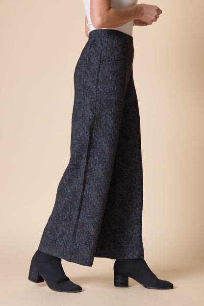 Person wearing dark gray wide-leg pants on a beige background