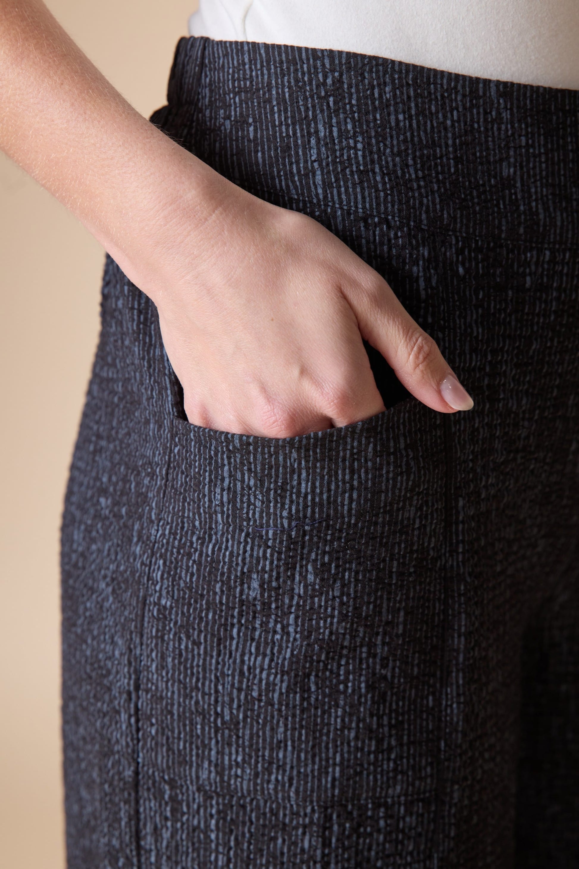 Person wearing dark gray textured pants with a beige background