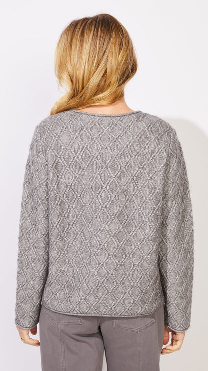 A woman viewed from the back wearing a light gray textured knit sweater with a diamond pattern and gray pants, set against a plain white background.