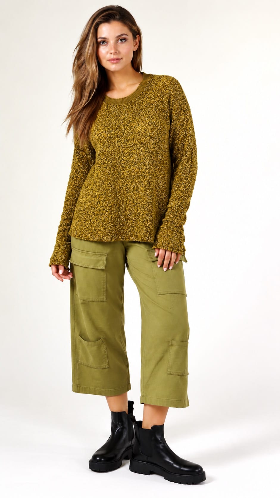 A woman modeling a textured olive green knit sweater and matching olive green cargo pants with black boots, photographed against a plain white studio background.