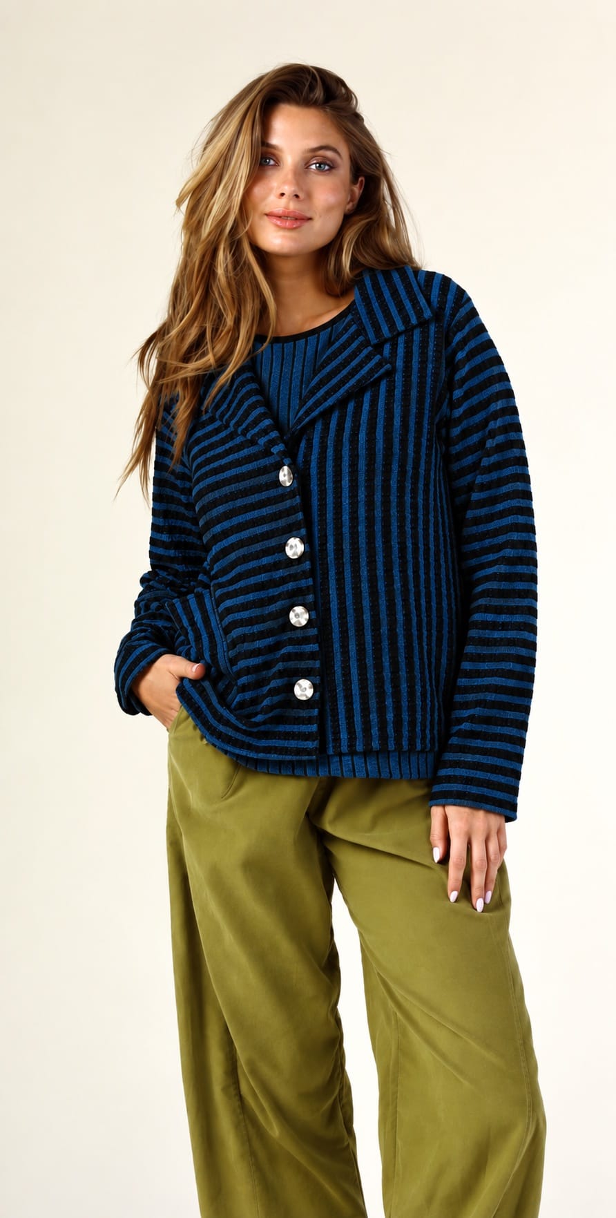 A woman modeling a navy blue and black vertically striped knit cardigan with silver buttons, paired with olive green wide-leg pants, against a plain off-white studio background.