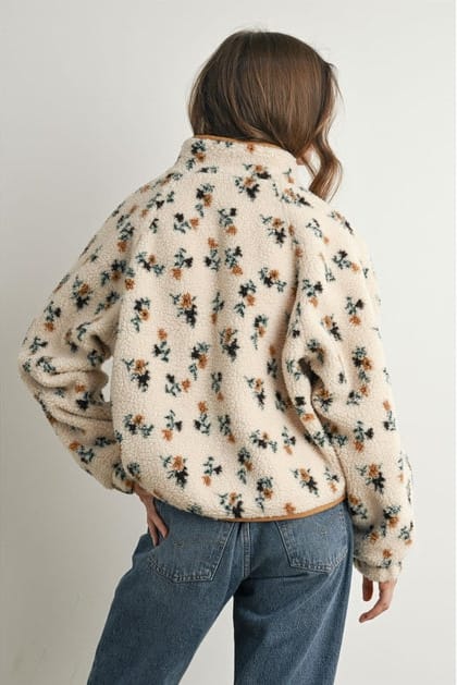 Person wearing a floral patterned jacket and blue jeans on a plain background