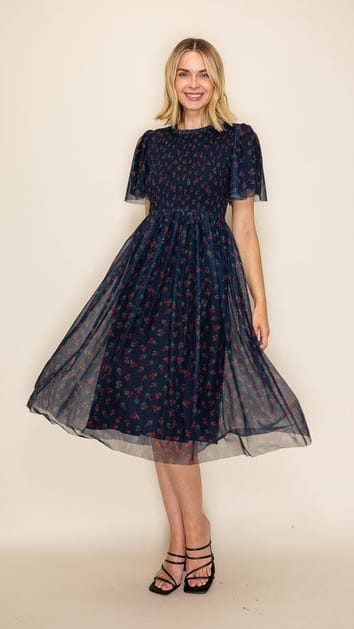 A woman modeling a dark navy blue midi dress with a small red and yellow floral pattern, featuring short puff sleeves and a flared skirt, set against a plain beige background.