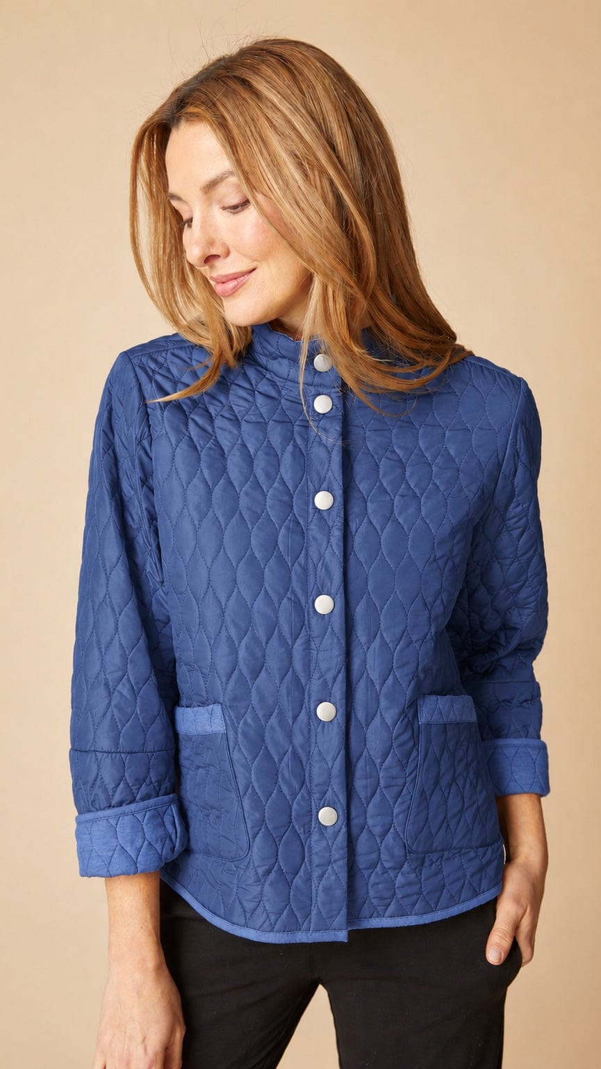 A woman wearing a blue quilted jacket with white buttons, shown from the waist up against a solid beige background.
