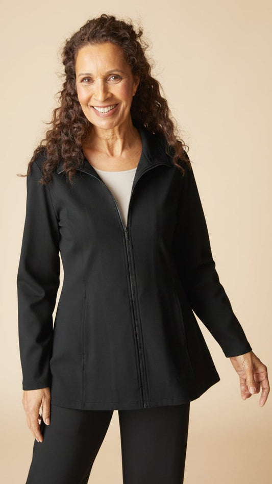 A smiling woman with curly brown hair models a black green zip-up jacket and matching pants against a solid beige studio background.