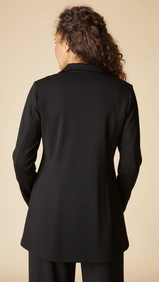 A woman viewed from the back wearing a black blazer and matching trousers against a plain beige studio background.