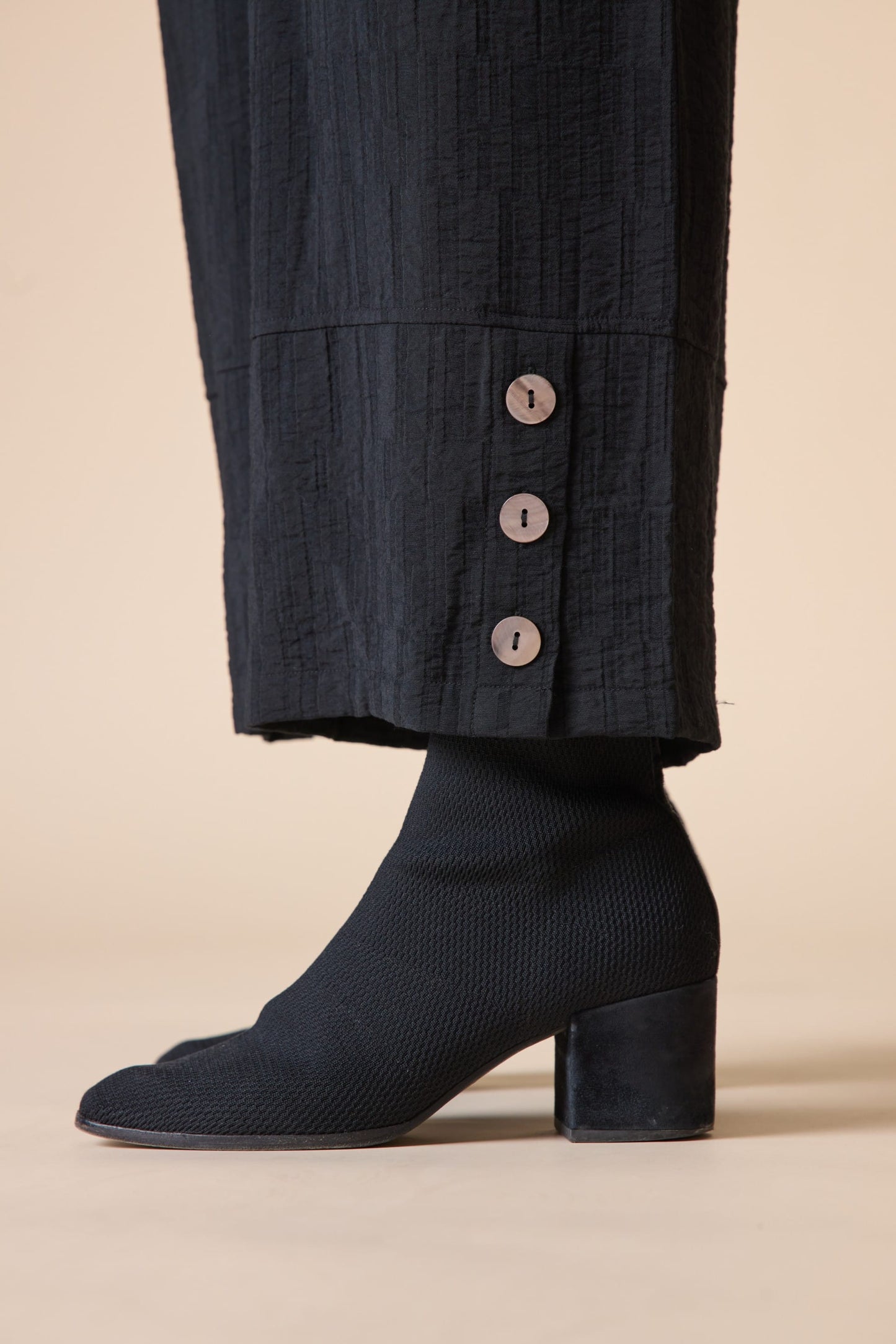 Black ankle boots worn with dark pants on a beige background