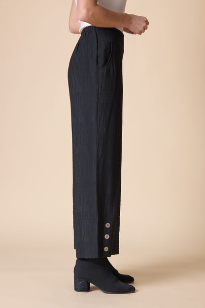Person wearing black pants with button details on a beige background