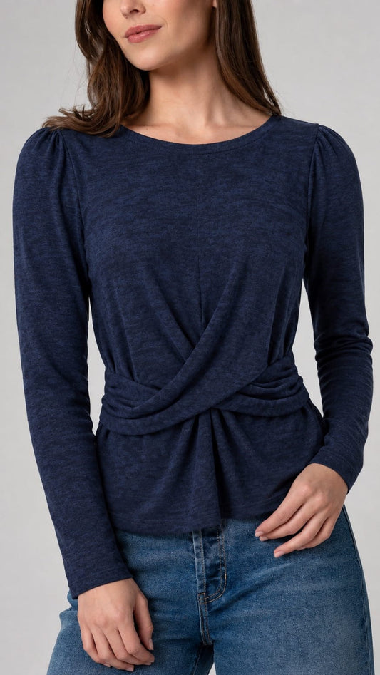 A woman wearing a navy blue long-sleeve top with a twisted wrap detail at the waist, paired with blue jeans, against a plain gray studio background.