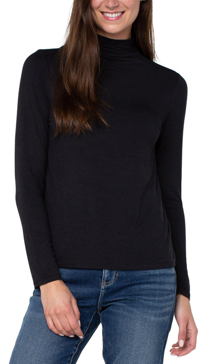 A woman wearing a black long-sleeve mock neck turtleneck top and blue jeans, shown from the chest down against a plain white background.