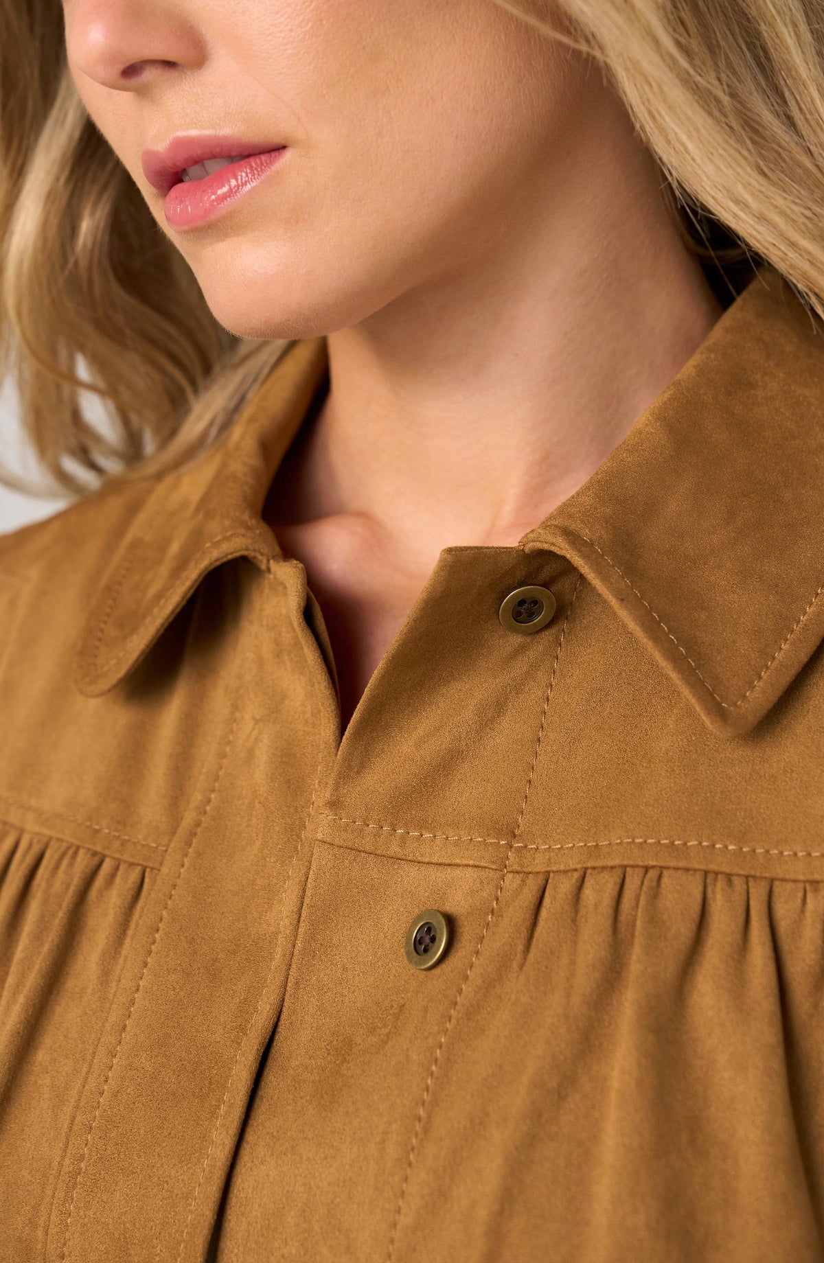 Close-up of a woman wearing a tan suede or faux-suede collared blouse with button front and gathered detailing.