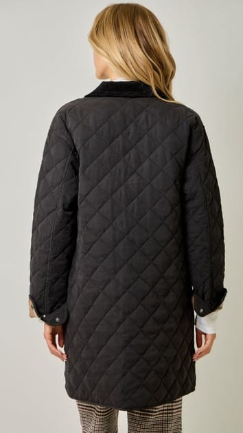 A woman shown from the back wearing a black diamond-quilted coat over a white collared shirt and plaid trousers, photographed against a plain light gray studio background.