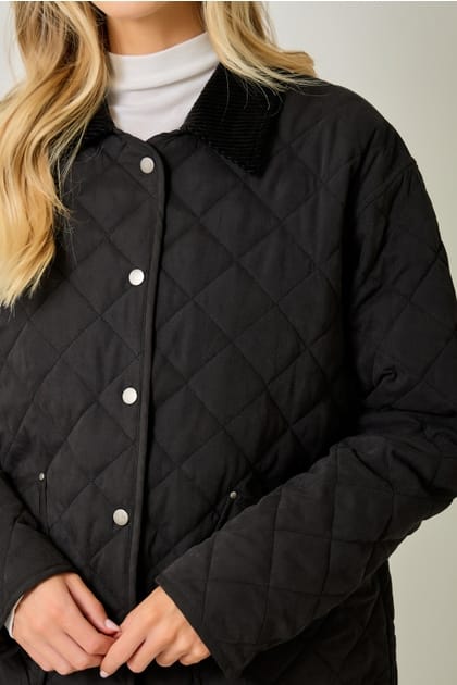 A close-up of a woman wearing a black quilted jacket with a corduroy collar and silver snap buttons, paired with a white turtleneck.