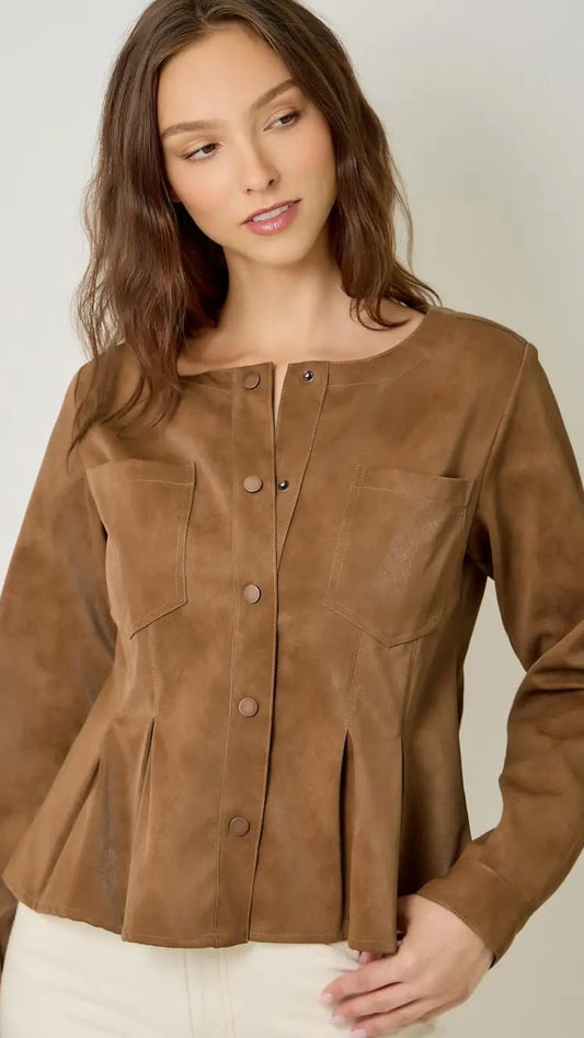 A woman wearing a brown faux-suede long-sleeve blouse with a button-down front and chest pockets, paired with off-white pants, against a plain light gray background.