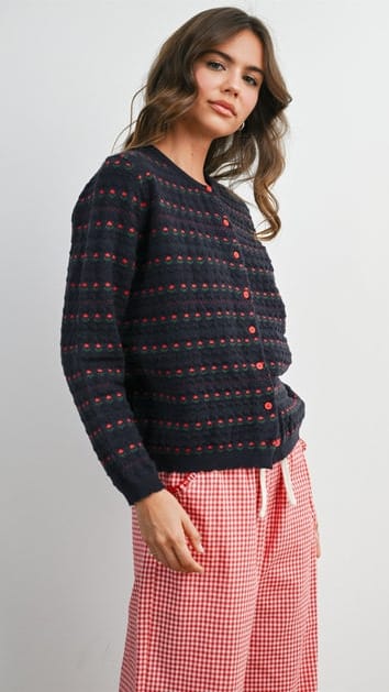 A woman wearing a dark navy textured knit cardigan with red and pink horizontal stripe patterns against a plain light gray background.