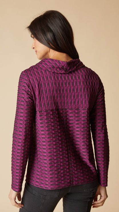 A woman shown from the back wearing a textured, patterned purple and pink hooded top against a solid beige background.