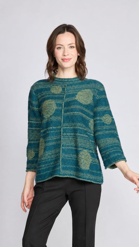 A woman modeling a teal and green textured knit jacket with a circular pattern, paired with black pants, against a light gray studio background.