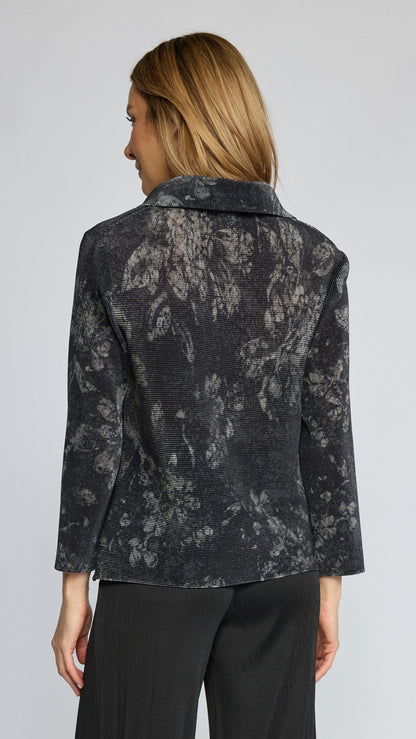 A woman shown from the back wearing a dark charcoal gray textured blazer with a lighter gray abstract floral pattern, paired with black trousers, against a light gray studio background.