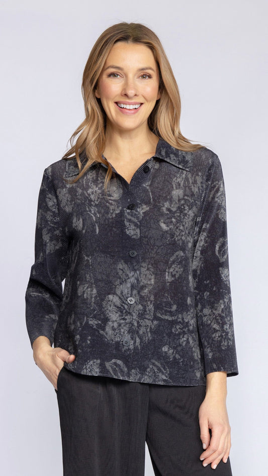 A woman modeling a long-sleeve button-up shirt with a dark gray and black abstract floral pattern, paired with black pants, against a light gray studio background.