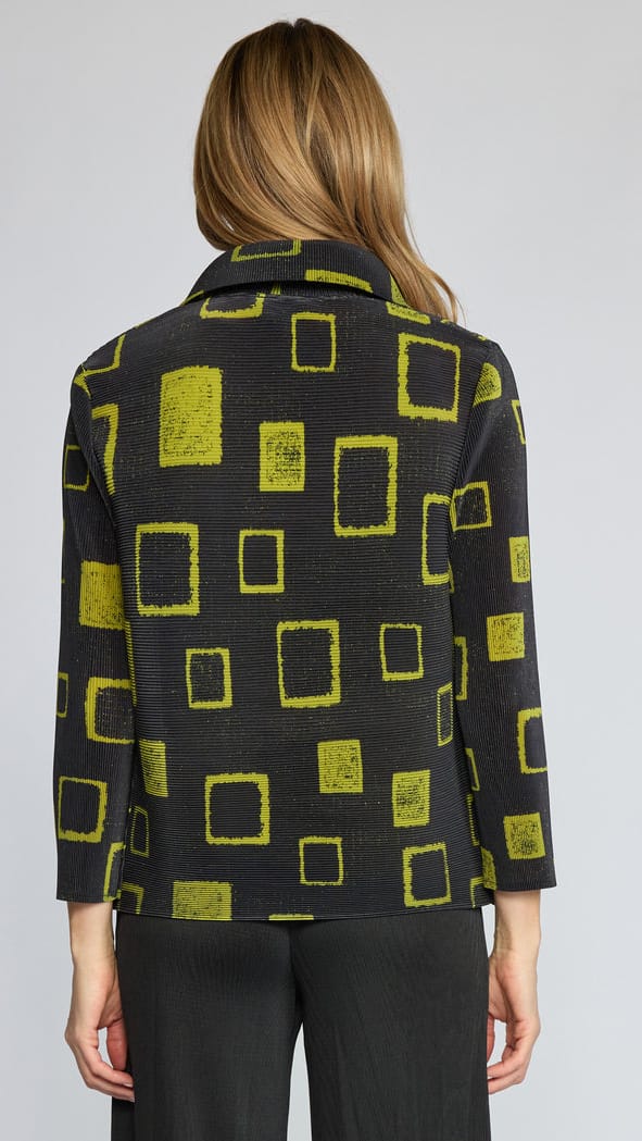 A woman viewed from the back wearing a black textured jacket with a yellow-green geometric square pattern, paired with black trousers, against a light gray studio background.