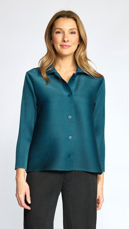A woman modeling a teal long-sleeve button-up shirt with a subtle textured sheen, paired with black pants, against a light gray studio background.