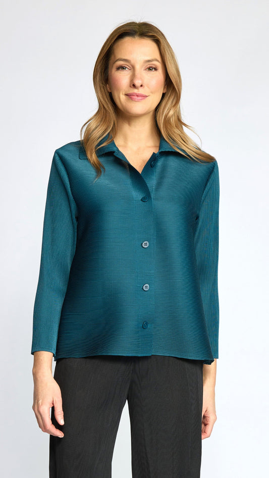 A woman modeling a teal long-sleeve button-up shirt with a subtle textured sheen, paired with black pants, against a light gray studio background.